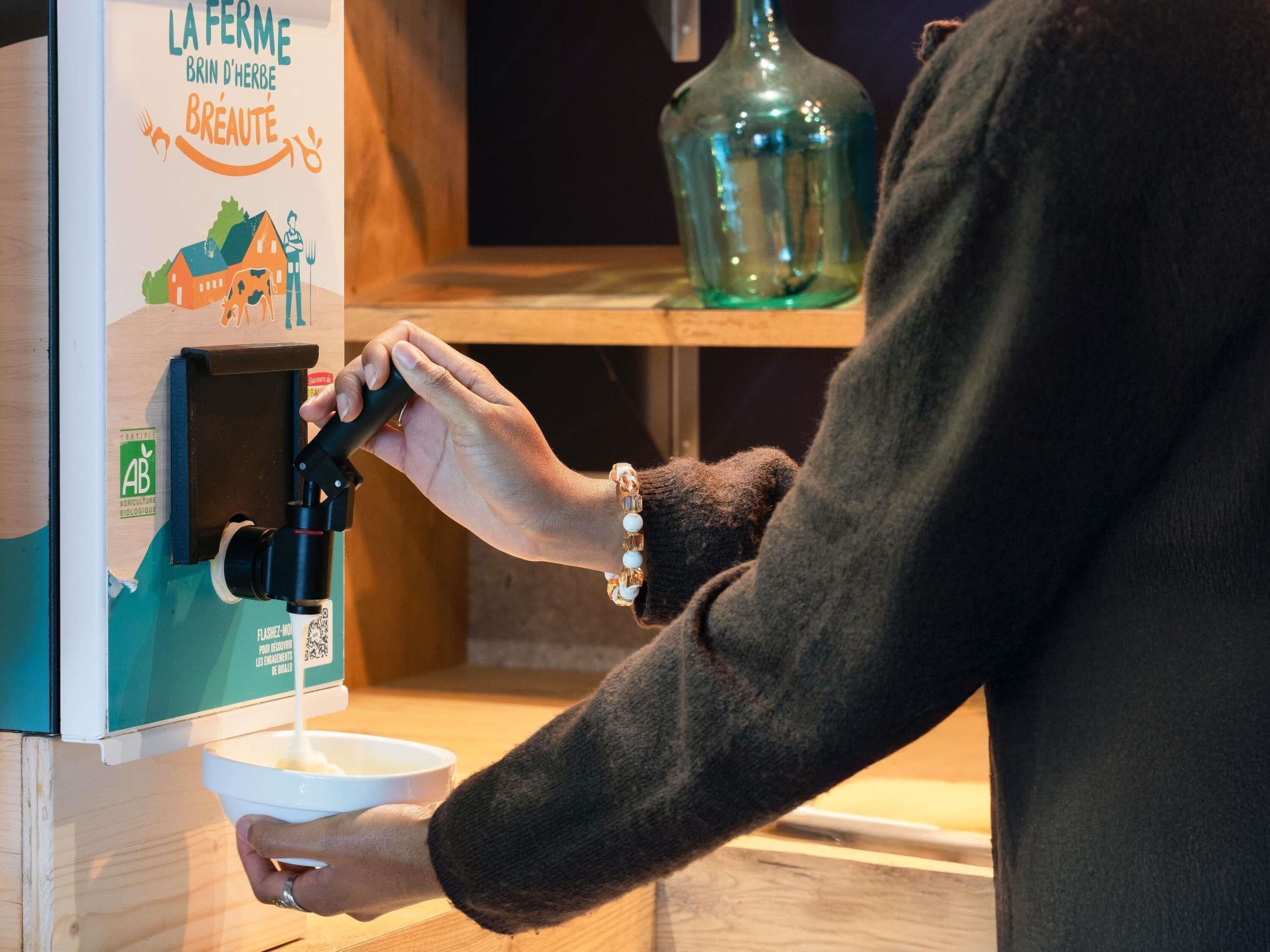 A person using a coffee machine with a label reading 'LA FERME BRIN D'HERBE BREAUUTE.'