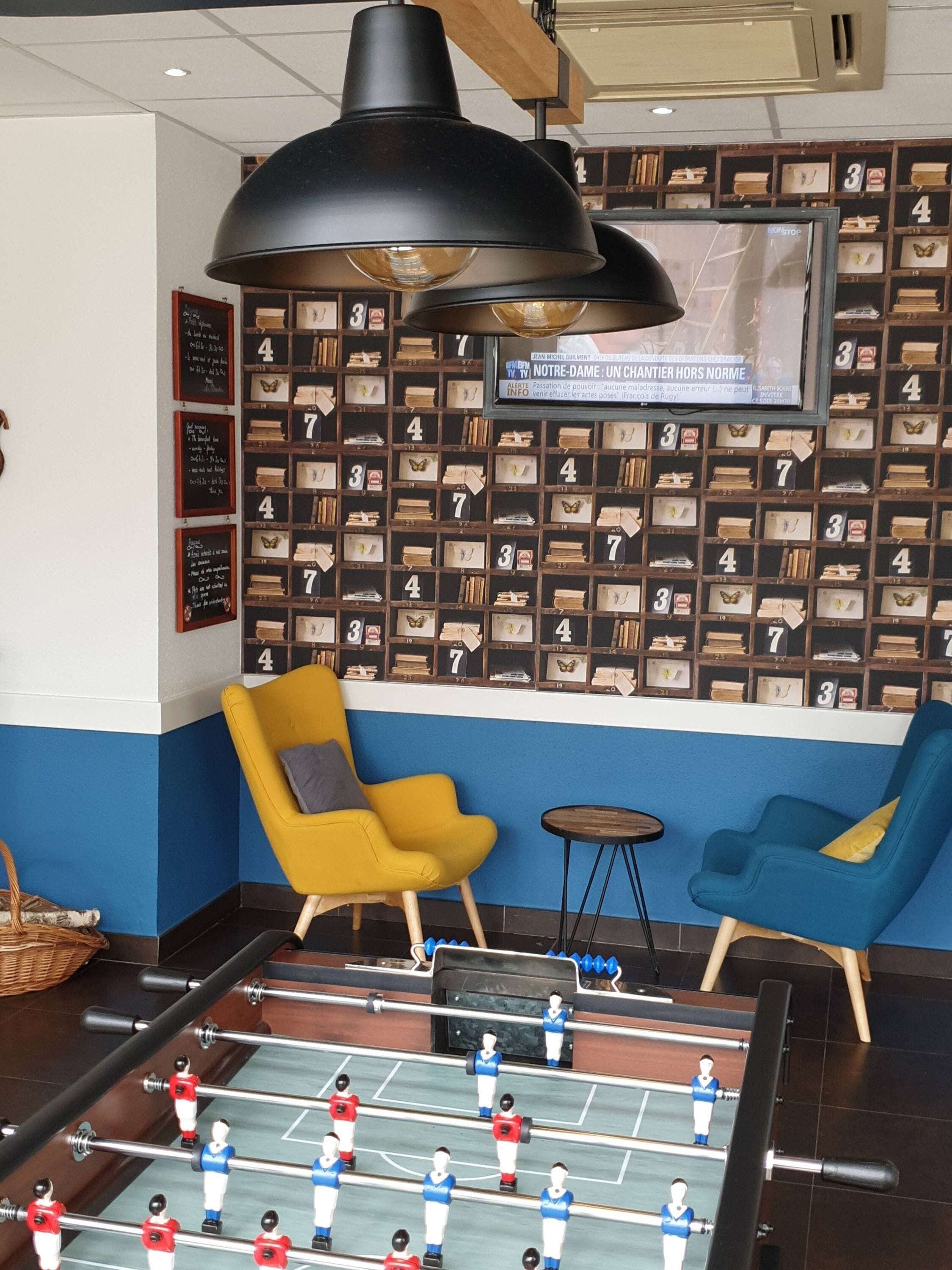 A room with a foosball table, two chairs, a large pendant light, and a wall with numbered shelves.