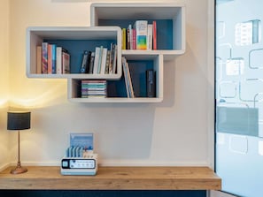 Una estantería de pared con libros, una estación de carga y una lámpara.