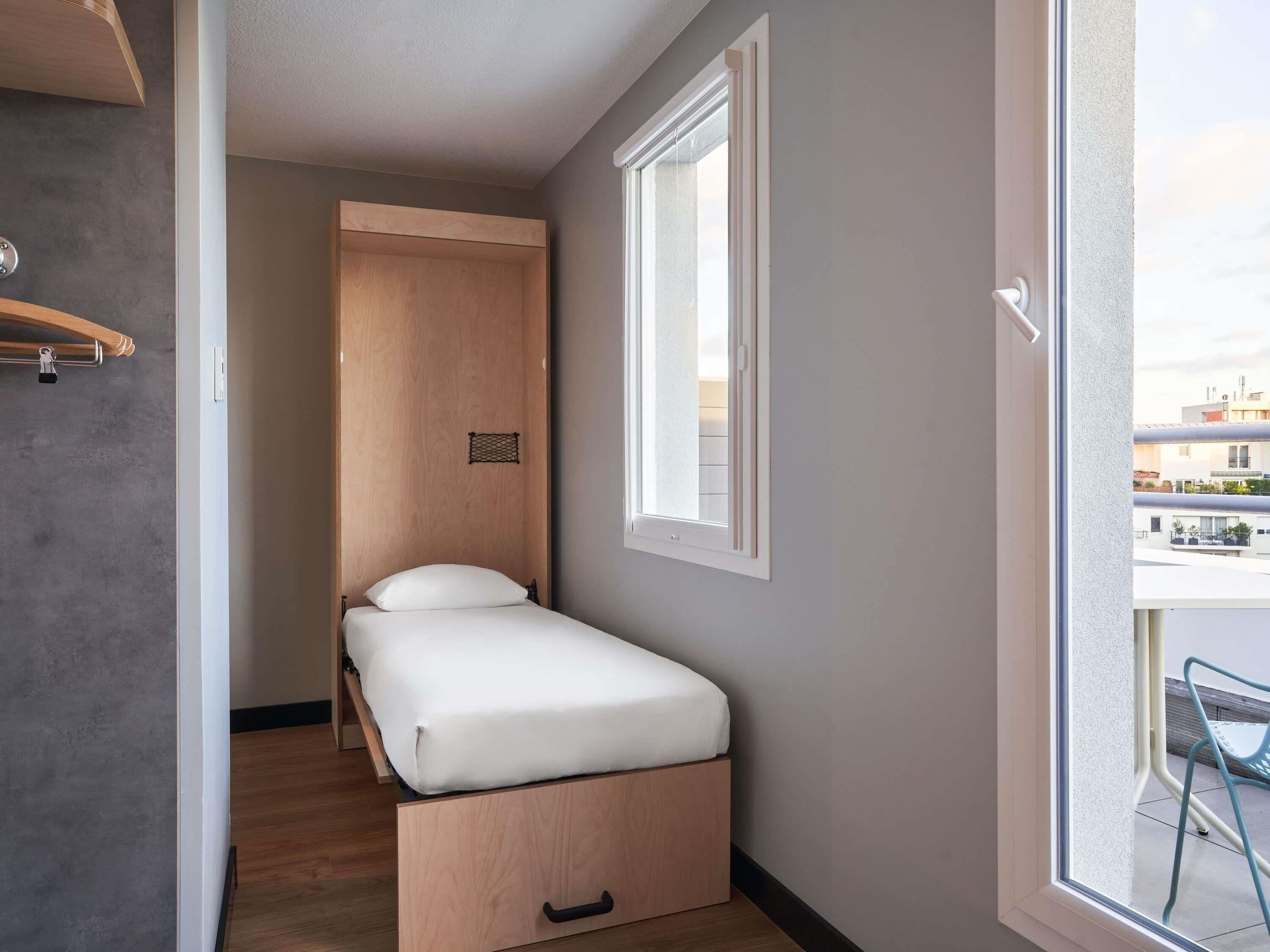 Un dormitorio pequeño con una cama individual, un armario de madera, un ventanal y vistas al balcón.
