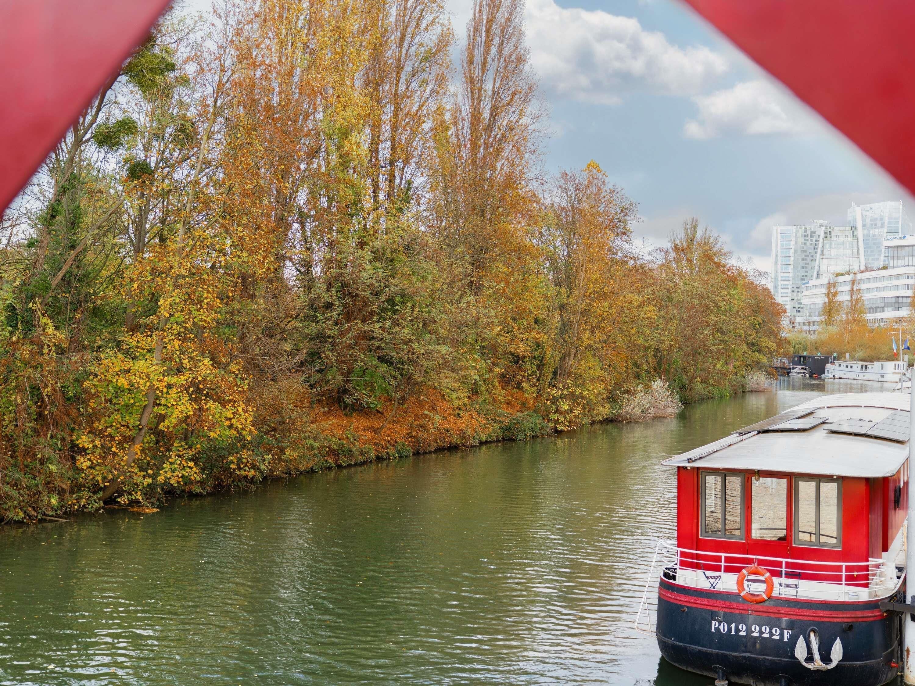 A river with autumn foliage and a red boat docked on the right.