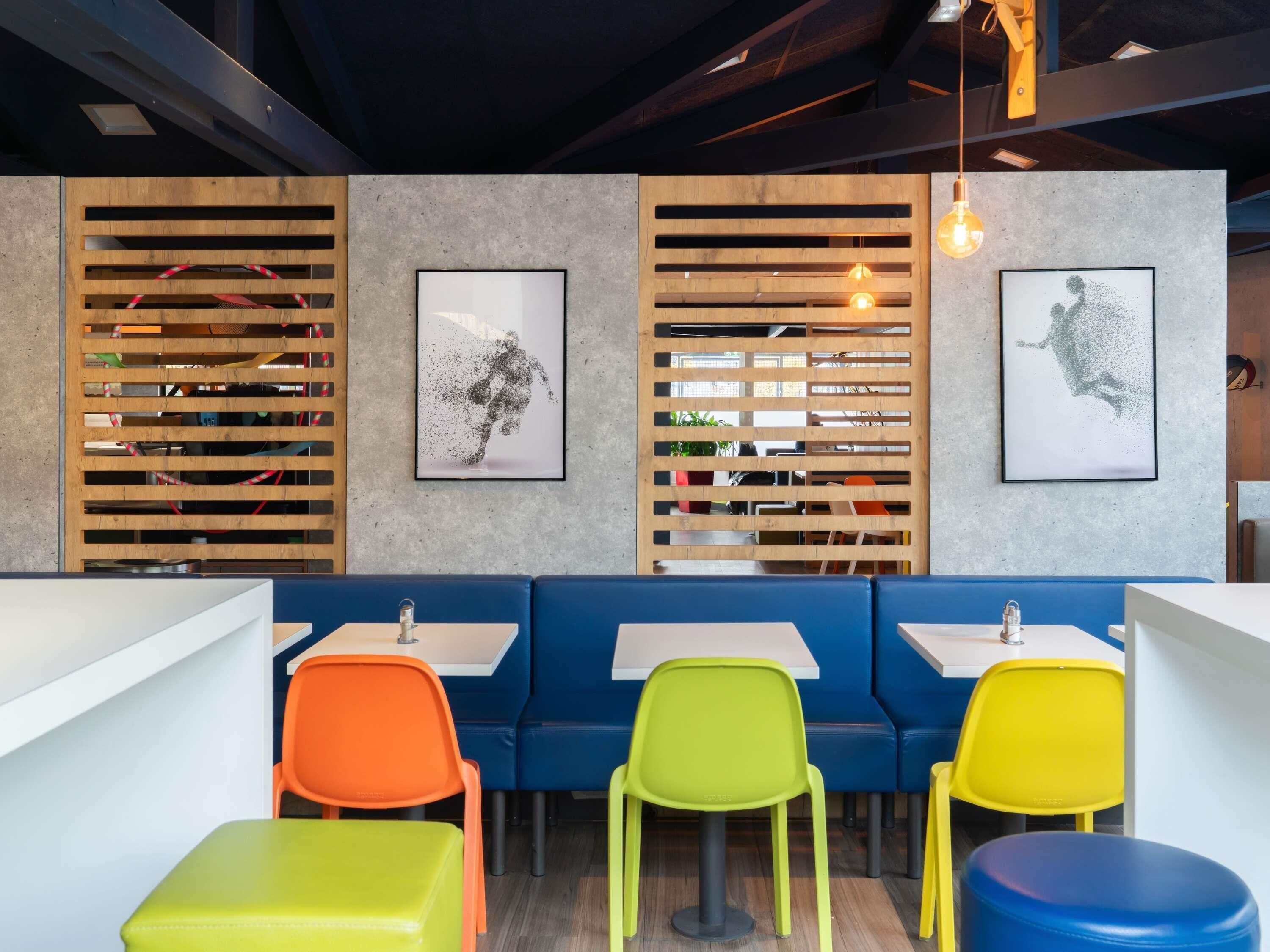 A modern restaurant interior with wooden slats, colorful chairs, and artwork on the walls.