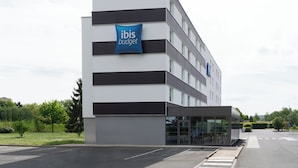 Un edificio moderno con un cartel que dice 'ibis budget'. Tiene techo plano, varias ventanas y entrada de cristal.