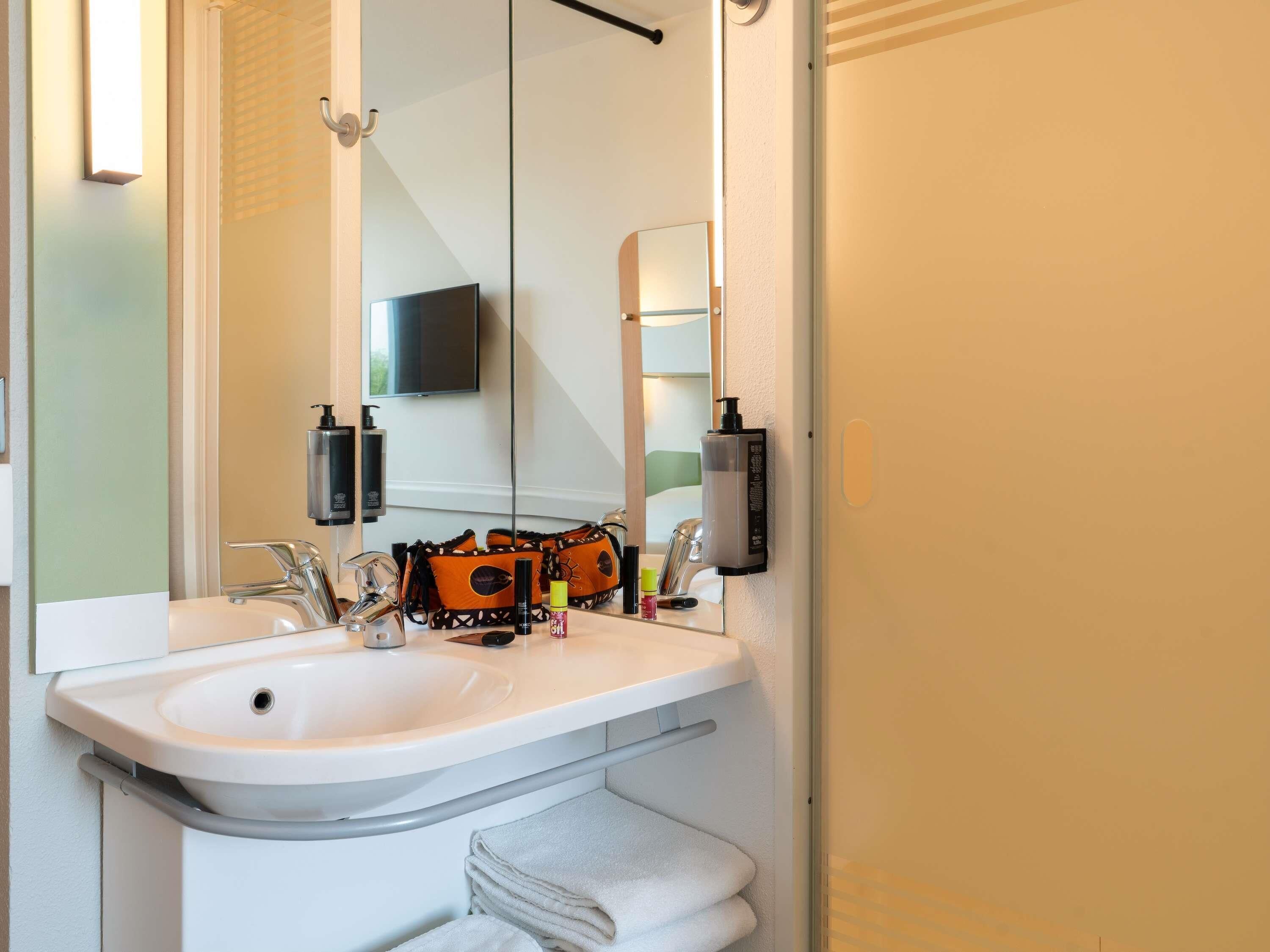 Een badkamer met een wastafel, spiegel, handdoekhouder en toiletartikelen.