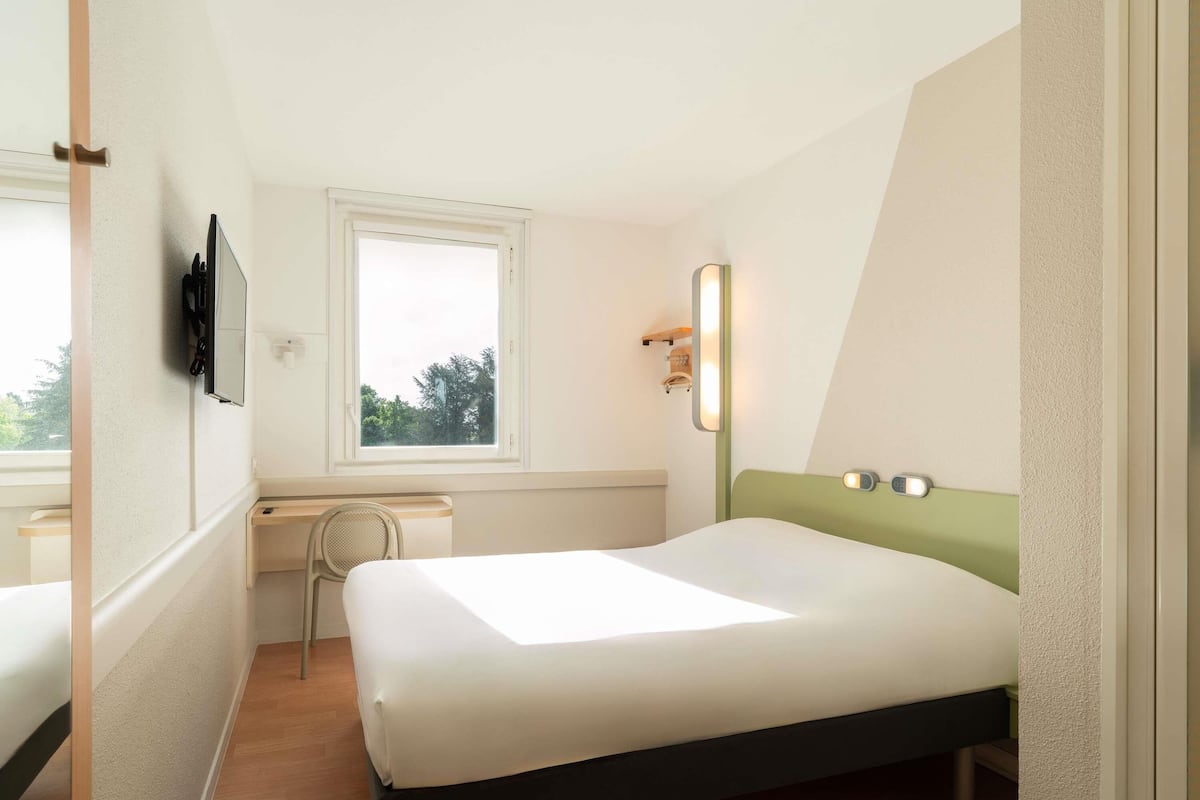 A bedroom with a bed, a window, a desk, and a mirror.