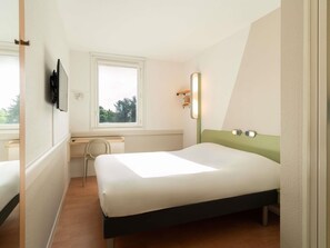 Une chambre à coucher avec un lit, un bureau, une chaise, une fenêtre et un miroir.