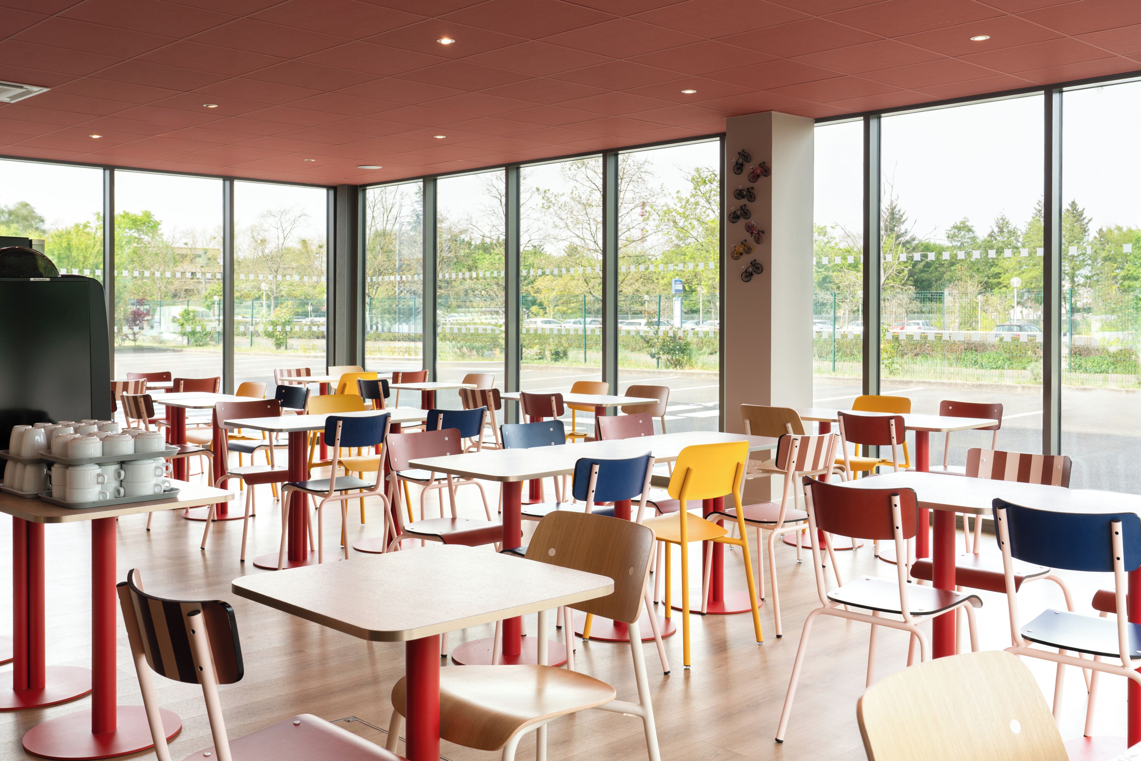 Un vaste espace de restauration intérieur, doté de nombreuses tables et chaises, et de grandes fenêtres offrant une vue sur l’extérieur.