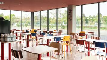 Un vaste espace de restauration intérieur, doté de nombreuses tables et chaises, et de grandes fenêtres offrant une vue sur l’extérieur.