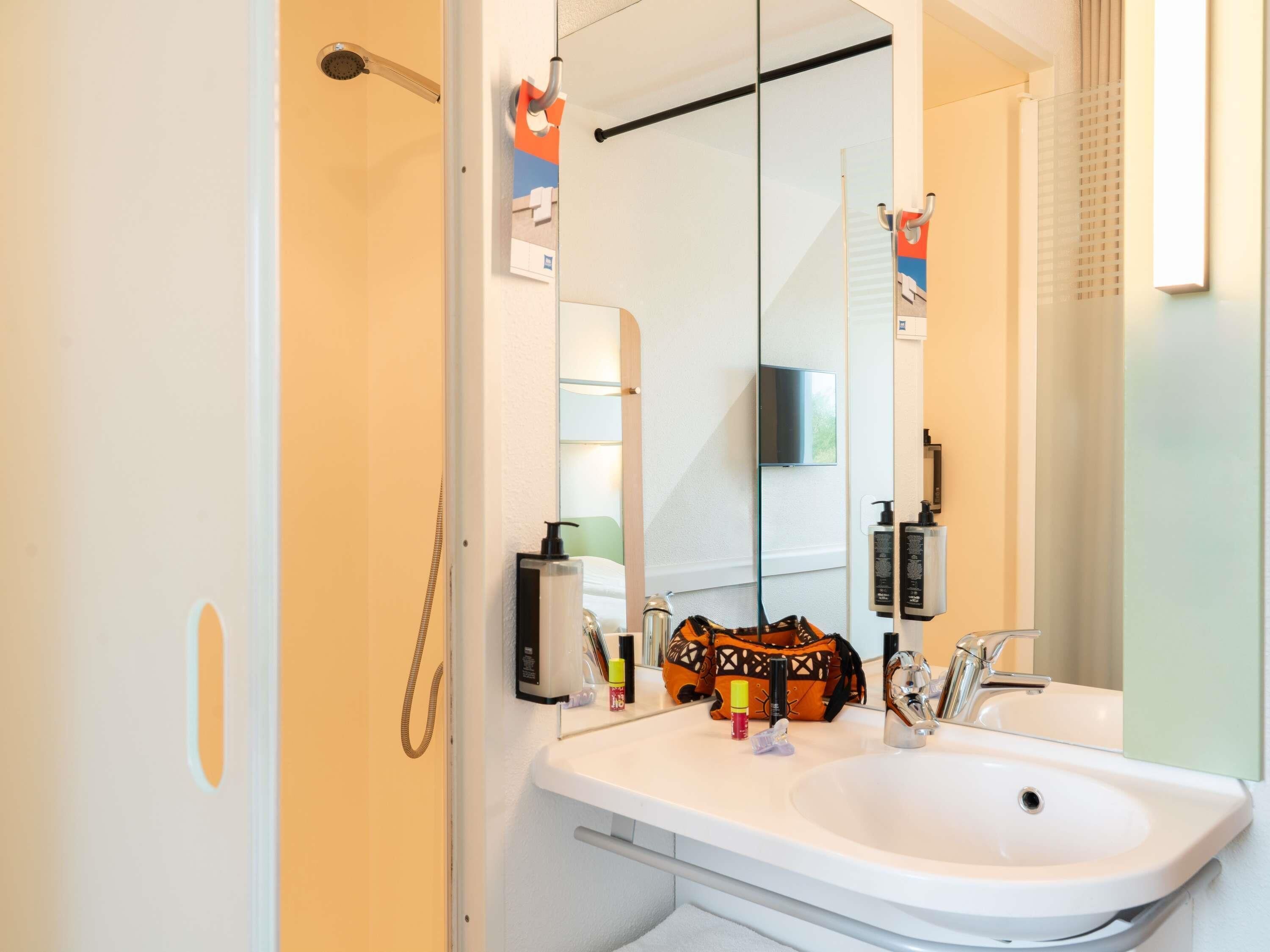 A bathroom with a white sink, a handheld showerhead, a mirror, and a towel rack.
