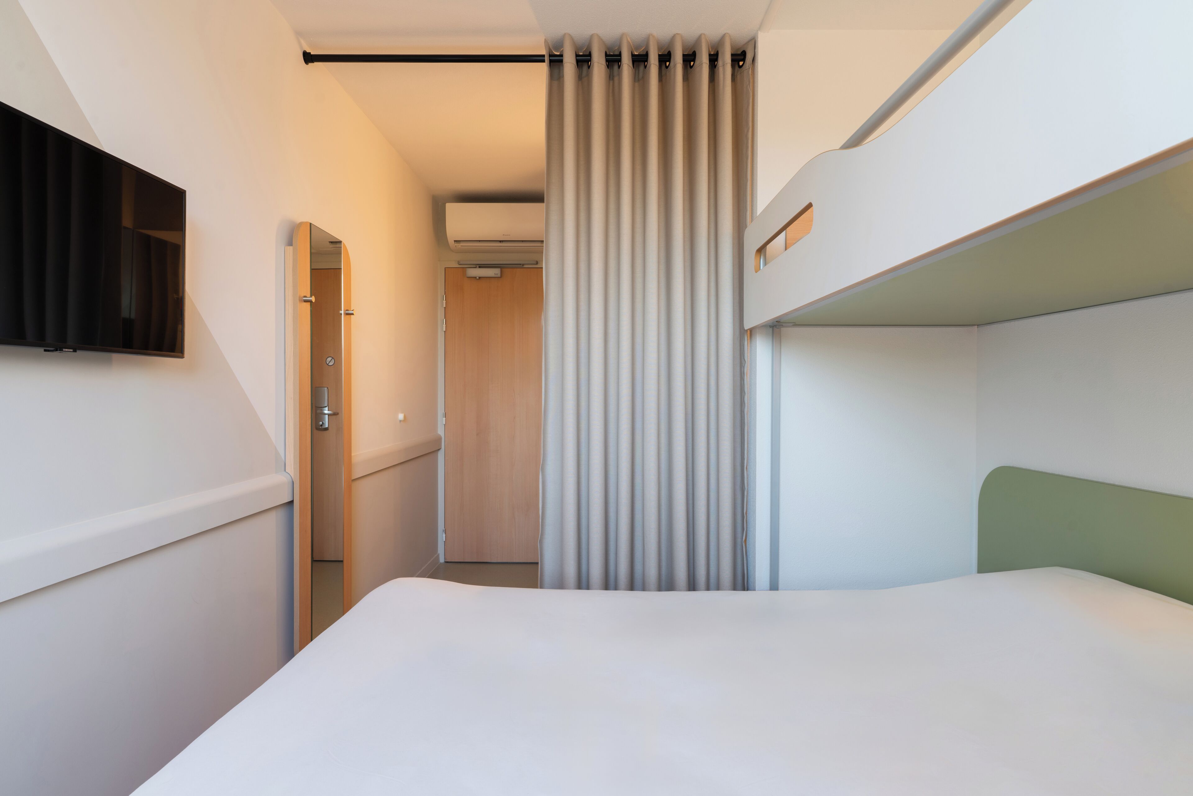 A modern hotel room with a bunk bed, a flat-screen TV mounted on the wall, and a walk-in closet.