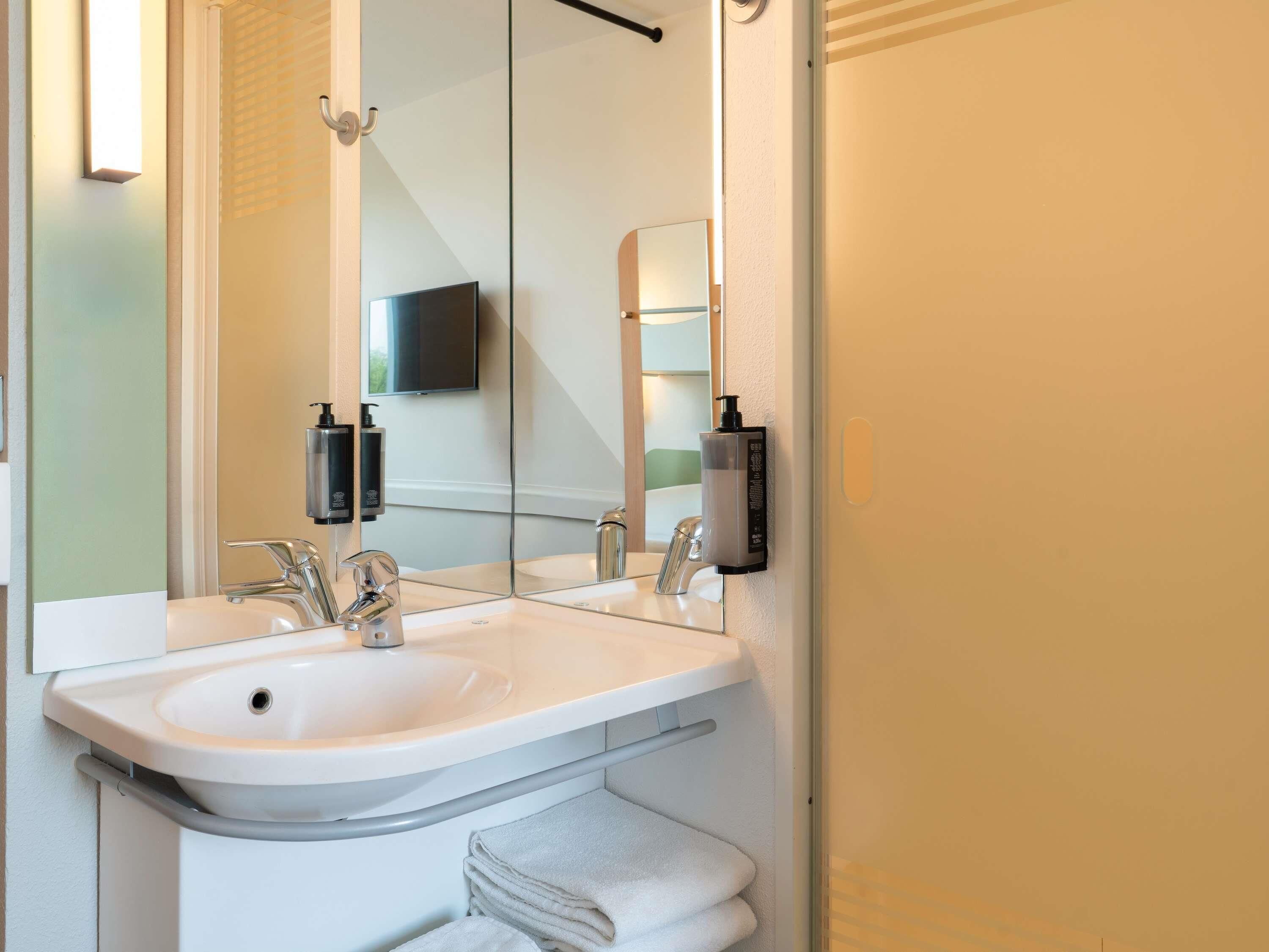 A modern bathroom with a white sink, two faucets, a mirror, and a towel rack.