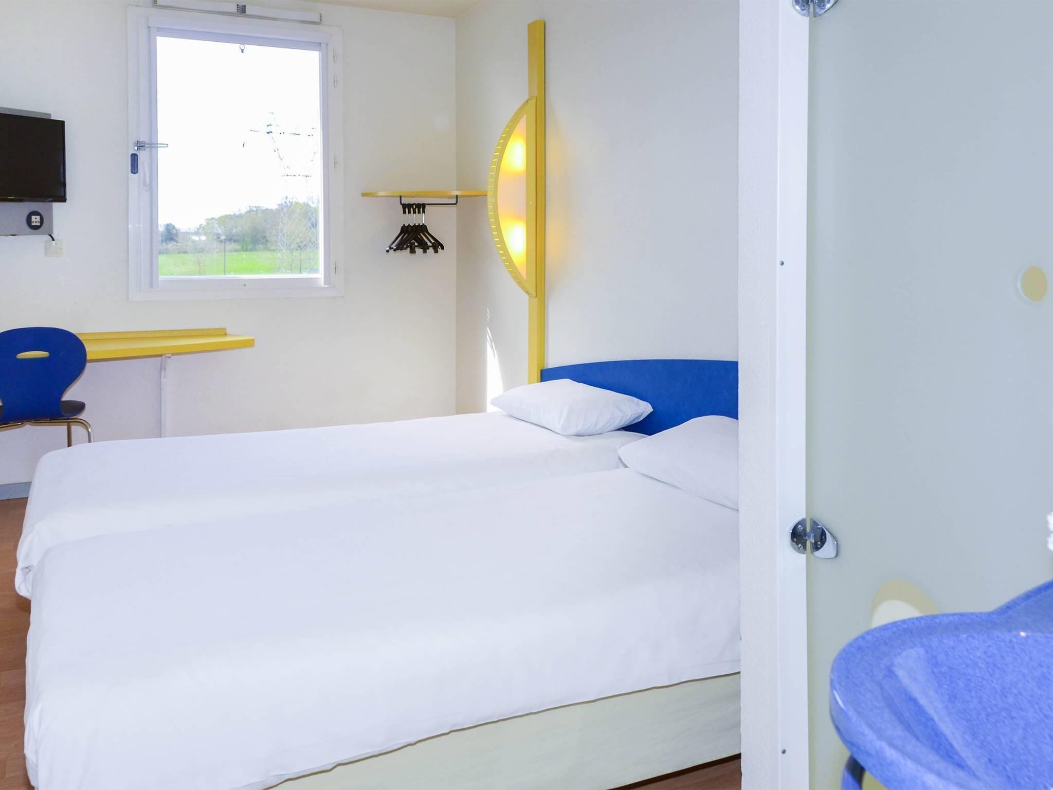 Ein Zimmer mit einem Bett, einem Schreibtisch, einem Stuhl, einem Fernseher und einem Fenster.