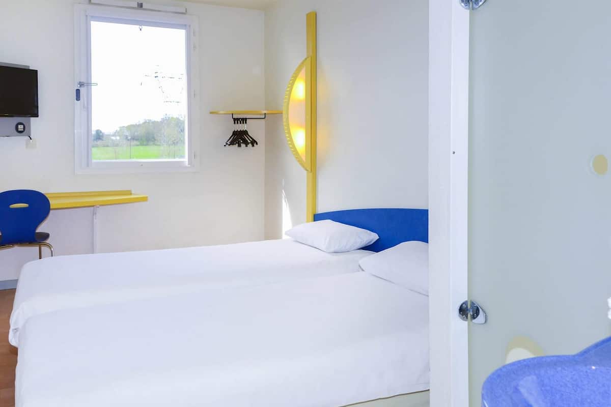 Ein Zimmer mit einem Bett, einem Schreibtisch, einem Stuhl, einem Fernseher und einem Fenster.