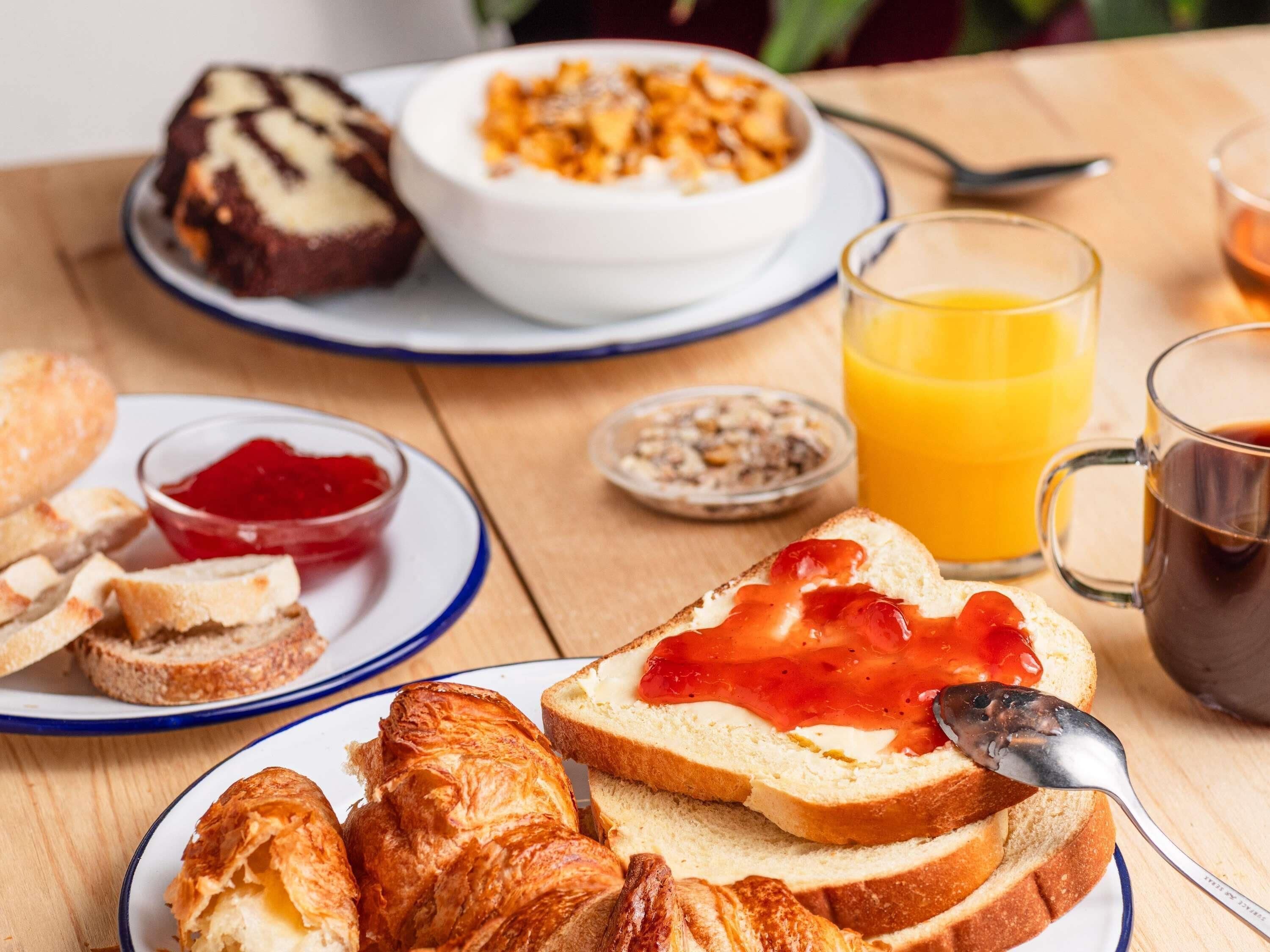 A breakfast setting with bread, jam, a bowl of cereal, and a glass of orange juice.