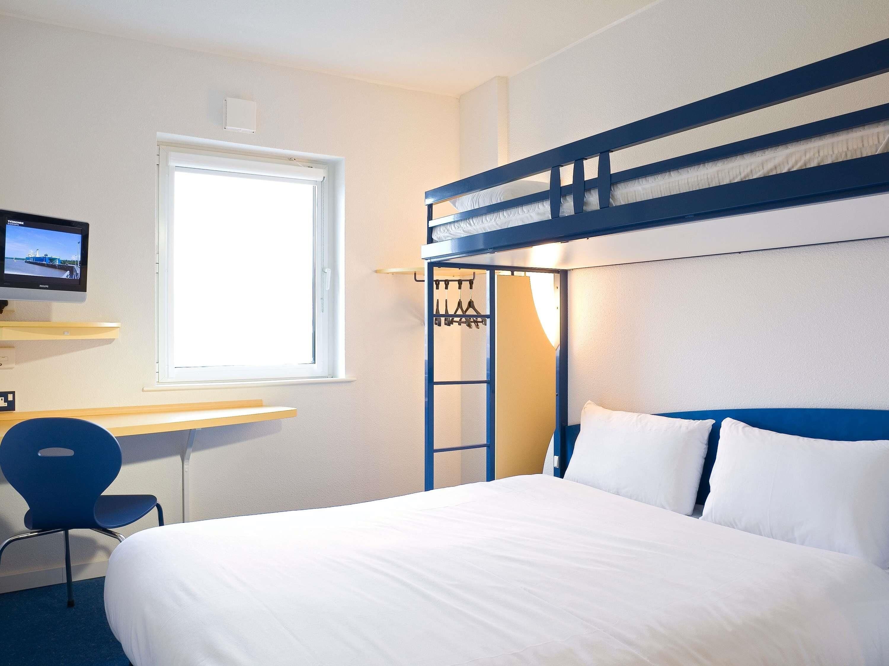 A bunk bed with white bedding, a desk with a chair, a television, and a window.