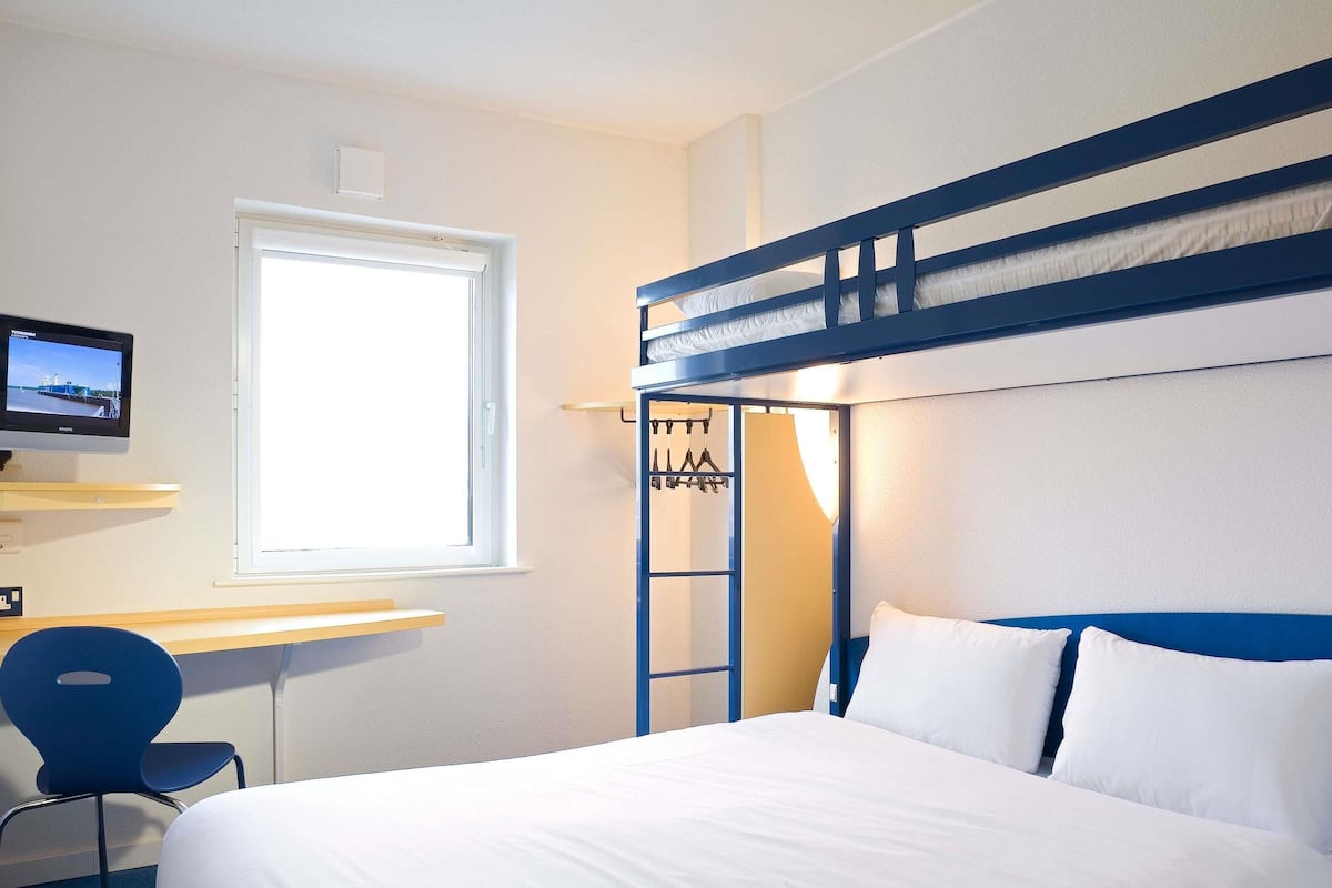 Ein Etagenbett mit weißer Bettwäsche, ein Schreibtisch mit Stuhl, ein Fernseher und ein Fenster.
