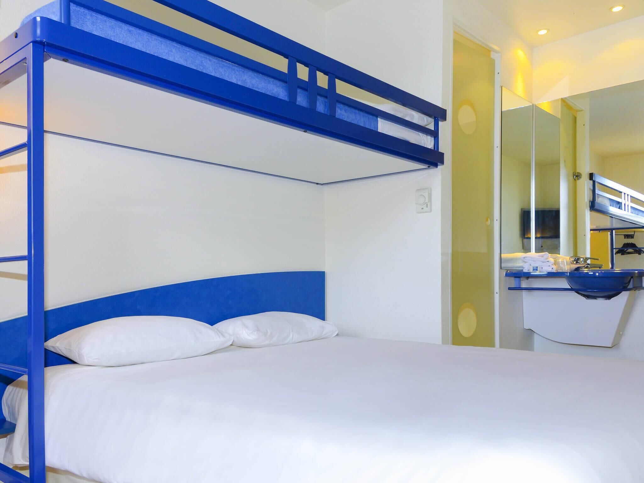 A bunk bed with white bedding, a blue headboard, and a bathroom with a sink and mirror.