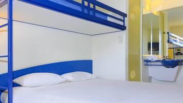 Una cama litera con ropa de cama blanca, un cabecero azul y un baño con lavabo y espejo.