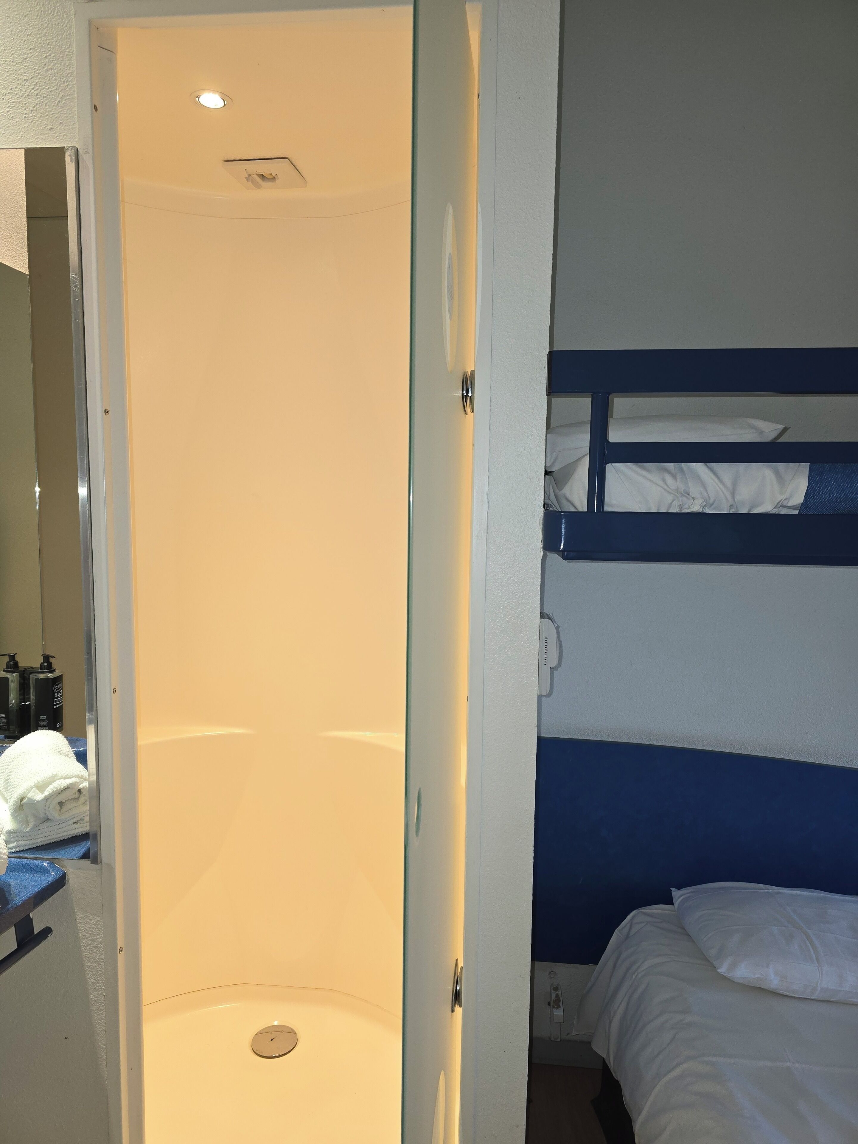 A hotel room with a shower, a bunk bed, and a mirror.