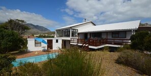 Una casa moderna de dos pisos con piscina, rodeada de paisaje natural y montañas.