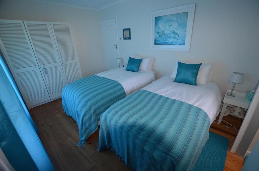 A room with two beds, each with a blue-striped bedspread, white pillows, and a framed picture on the wall.