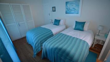 A room with two beds, each with a blue-striped bedspread, white pillows, and a framed picture on the wall.