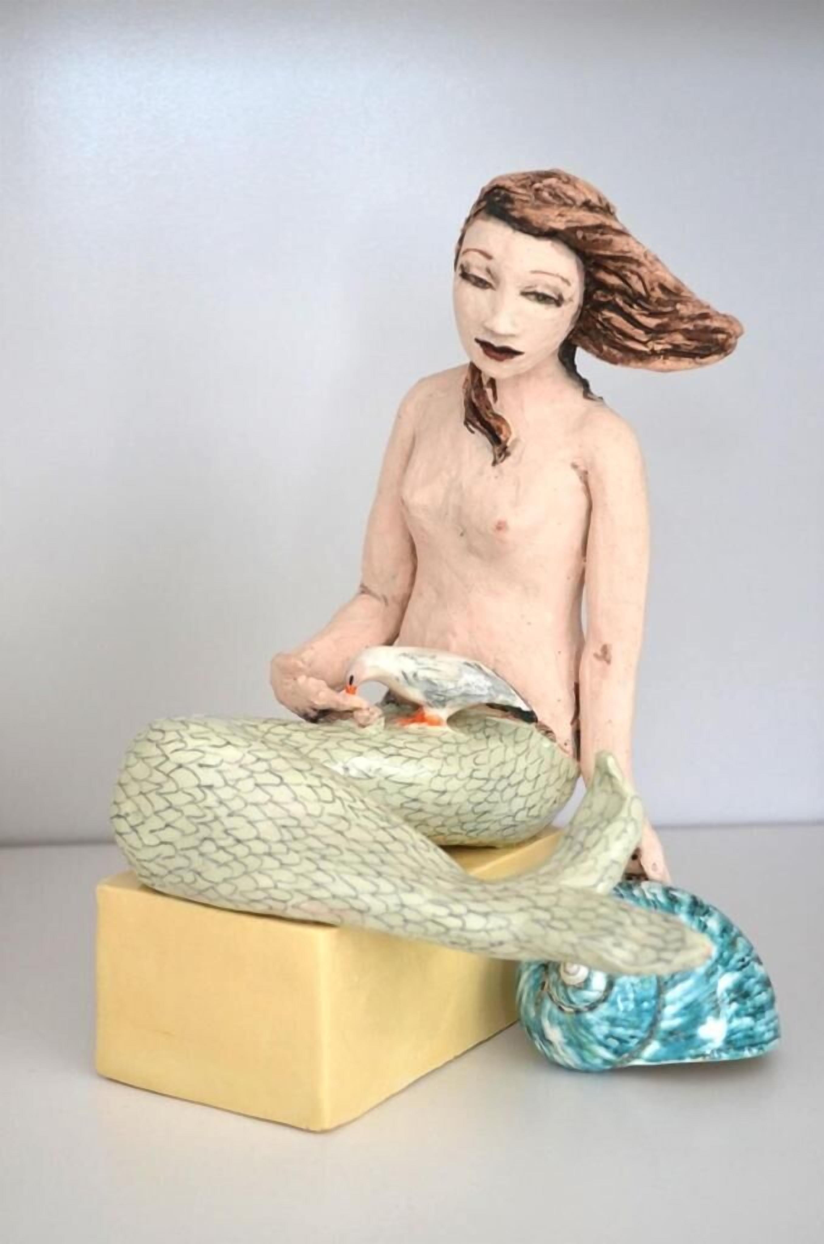 A figurine of a mermaid sitting on a golden block with a fish beside her.