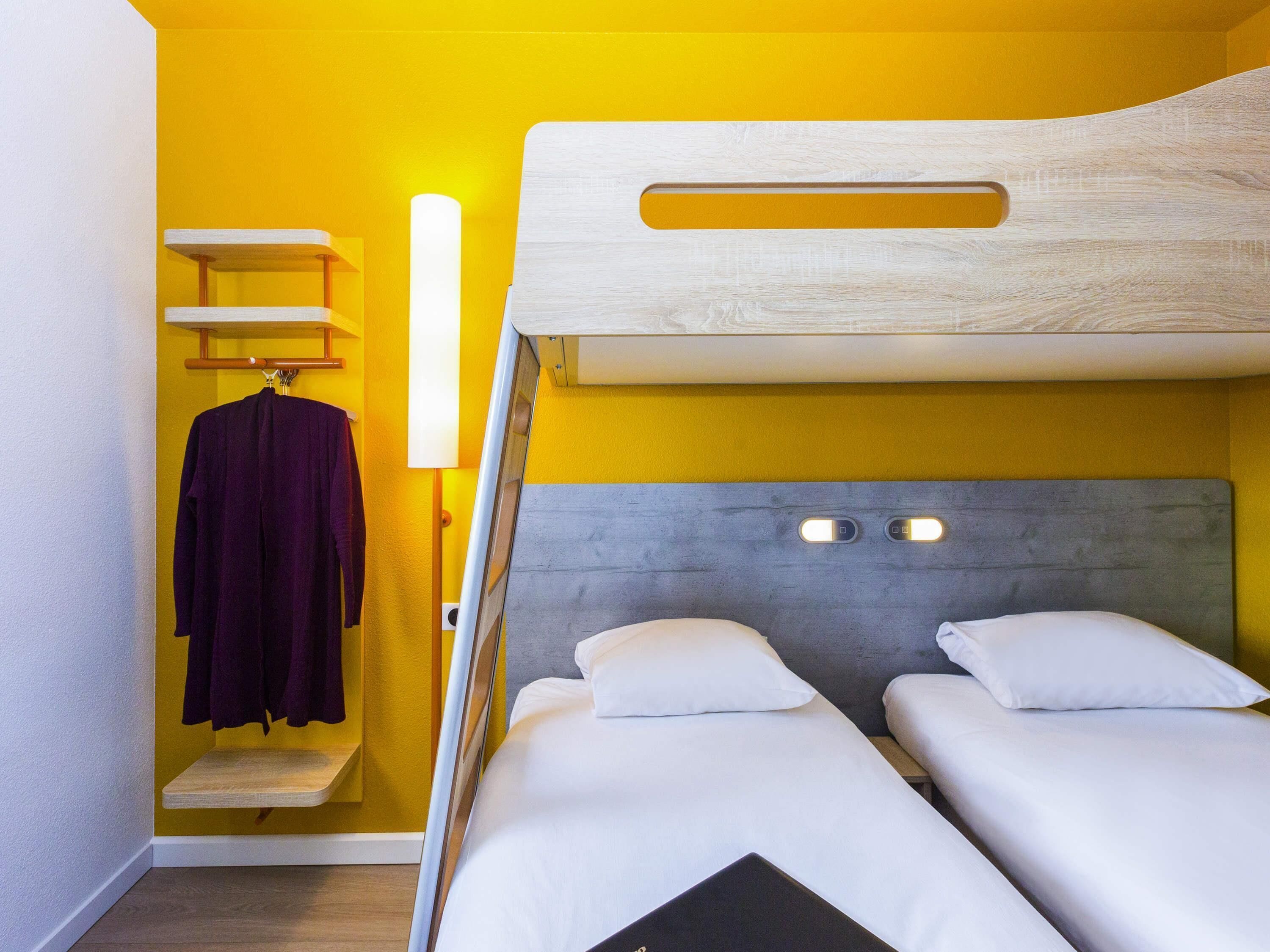 A room with a bunk bed, a small shelf with a robe, and a wall-mounted lamp.