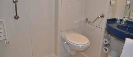 Un baño con inodoro blanco, lavabo azul y cabina de ducha con paredes de vidrio.