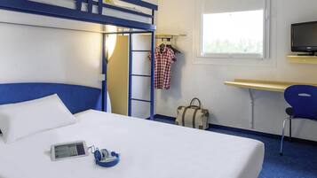 A hotel room with a bunk bed, a desk with a chair, a television, and a window.
