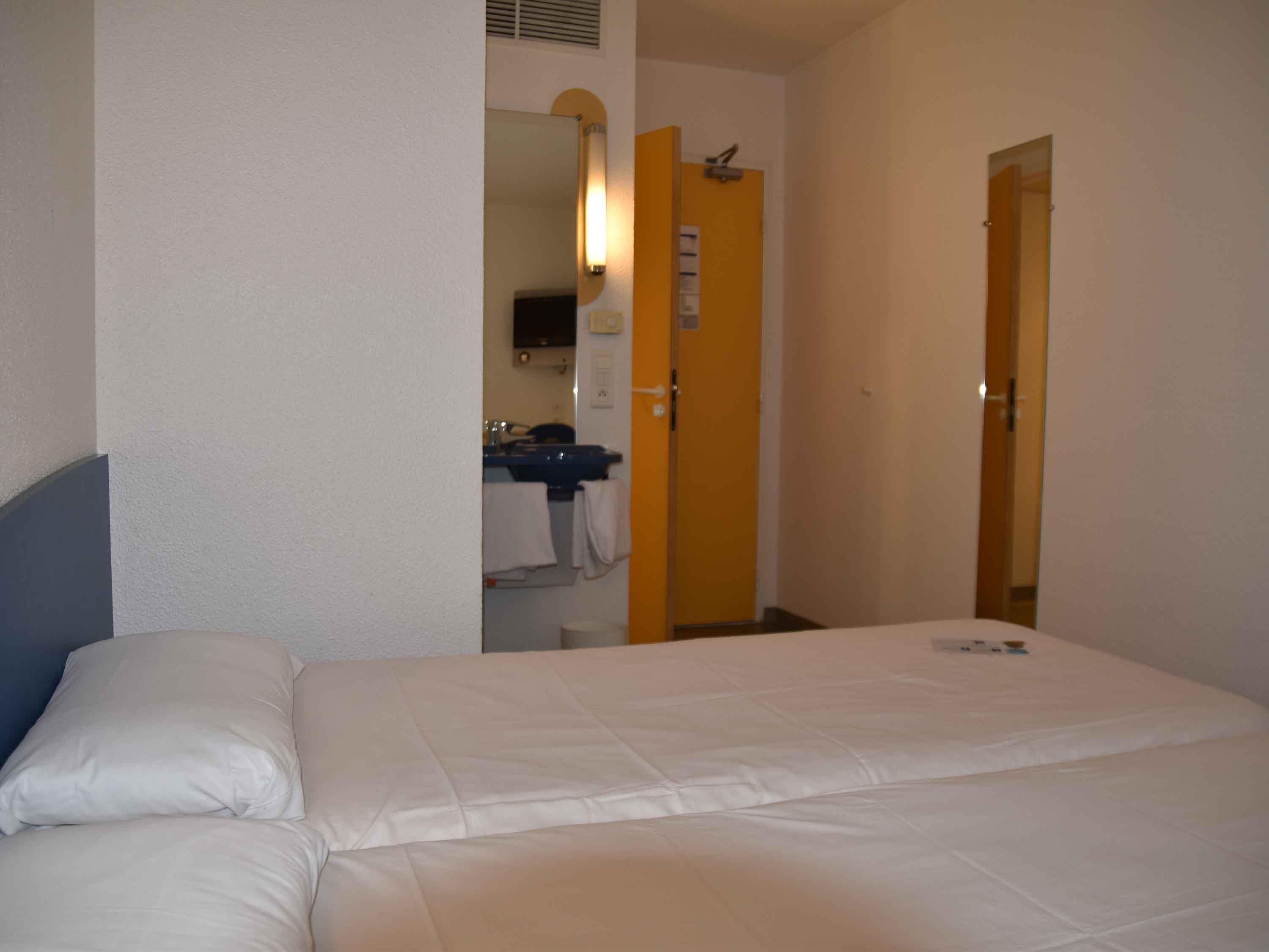 A hotel room with a bed, a bathroom with a sink and mirror, and a door leading to another room.