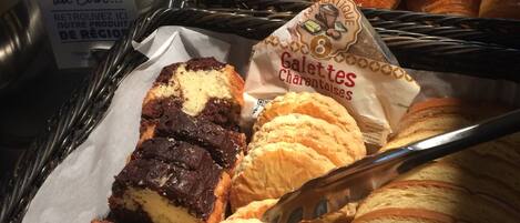 A display of assorted pastries and baked goods, including croissants, muffins, and a chocolate cake, arranged in a basket.