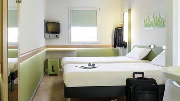 Quarto de hotel com duas camas, uma televisão, uma janela, uma escrivaninha, uma mala e um par de sapatos.