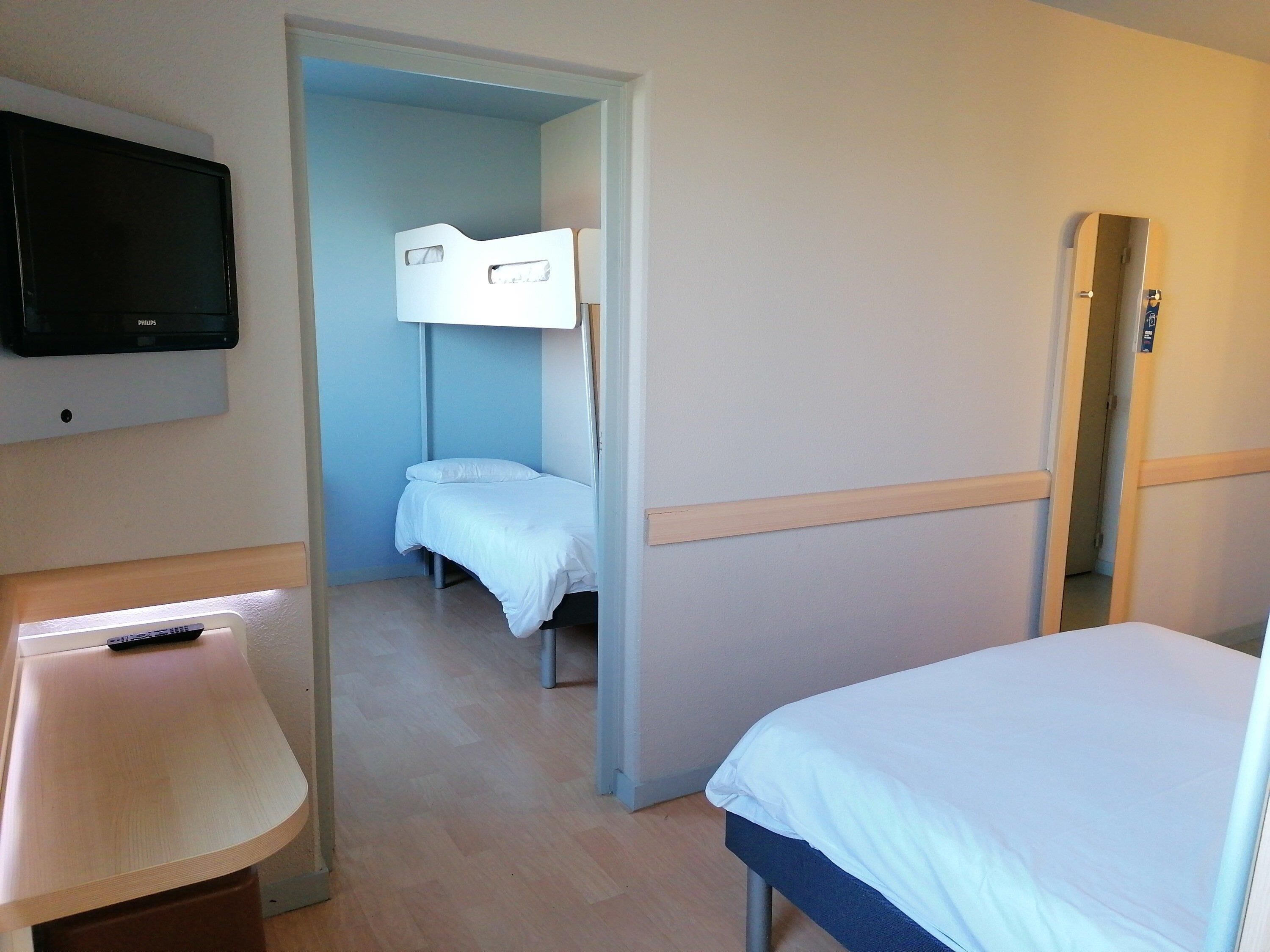 A hotel room with a bed, a desk, a television, and a door leading to another room.