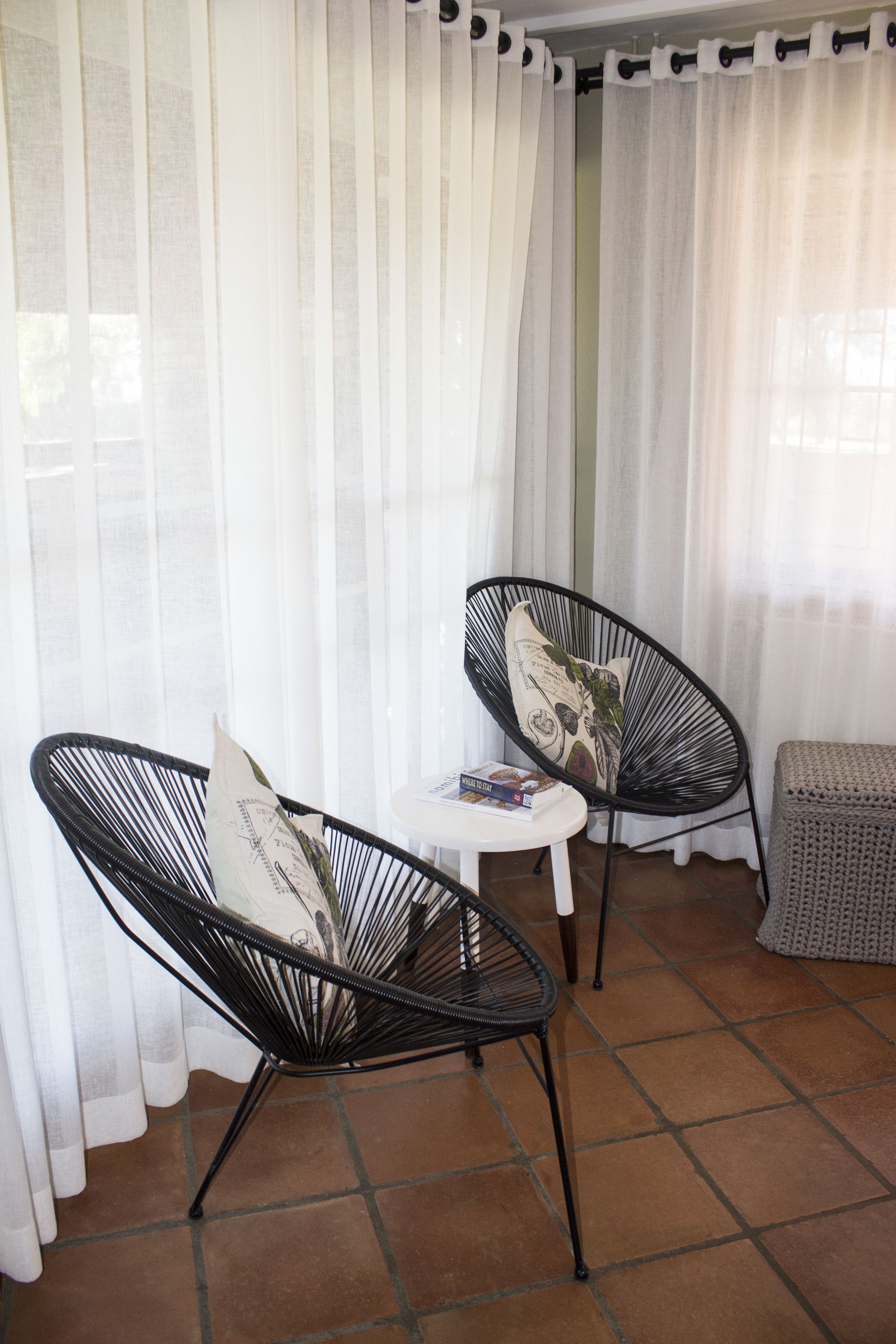 Deux chaises au design minimaliste, avec une structure en fil de fer noir et des coussins, une petite table blanche et un banc en osier.
