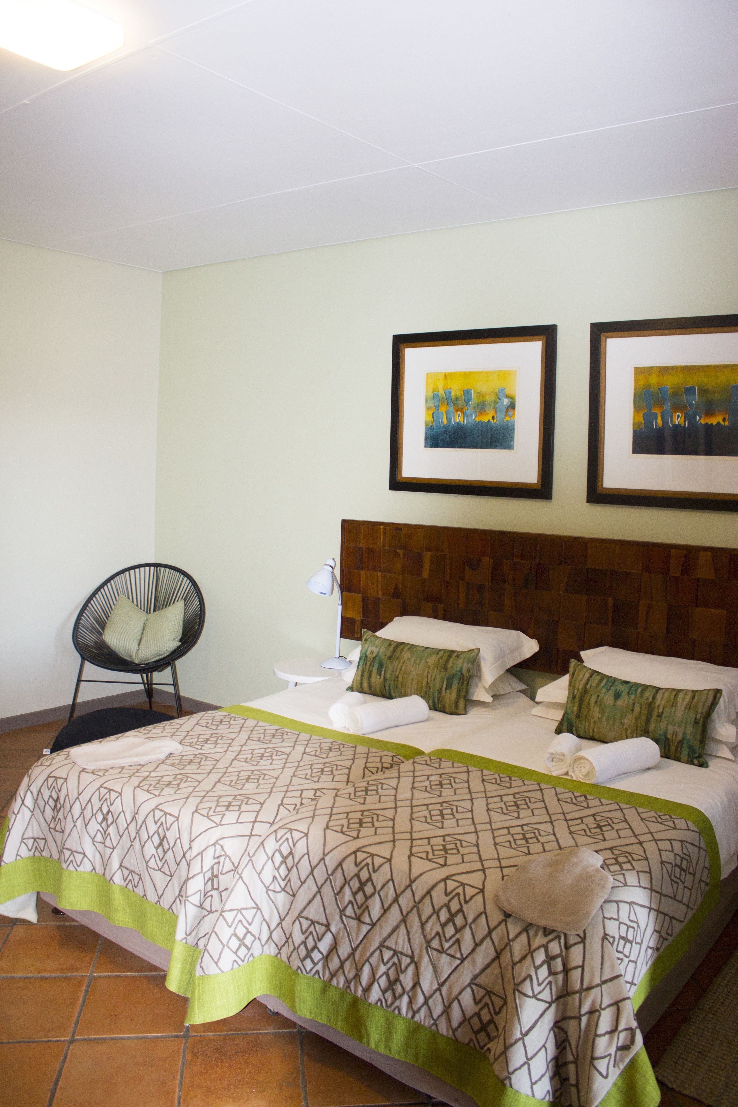 A hotel room with a bed, a chair, and two framed pictures on the wall.