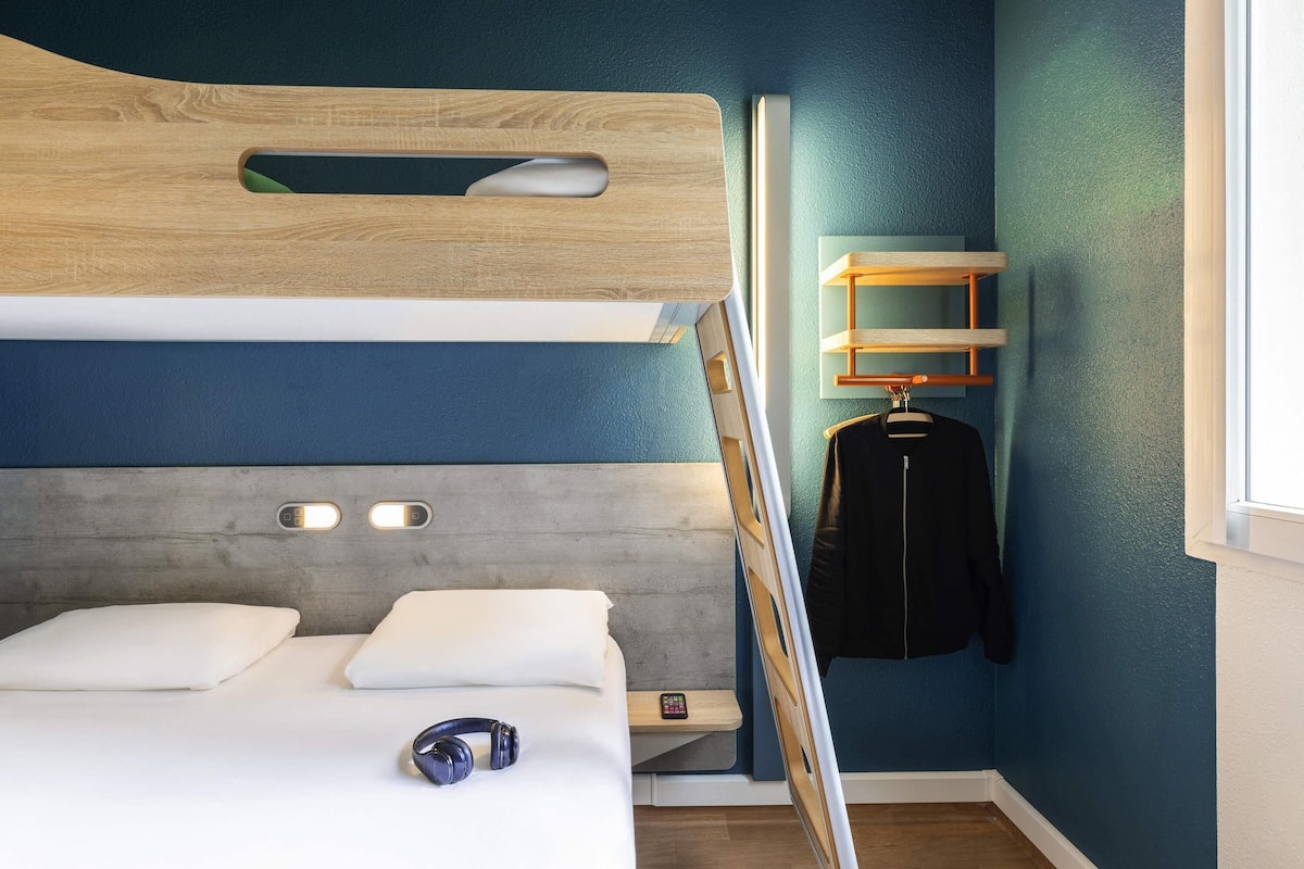 A bunk bed with a wooden headboard, a bedside table with a remote control, a pair of headphones on the bed, and a hanging jacket.