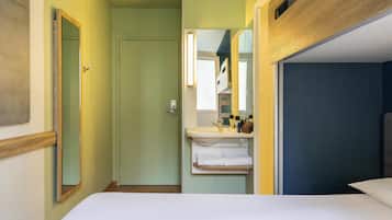 A compact hotel room with a bed, a bathroom with a sink and mirror, and a door leading to another room.