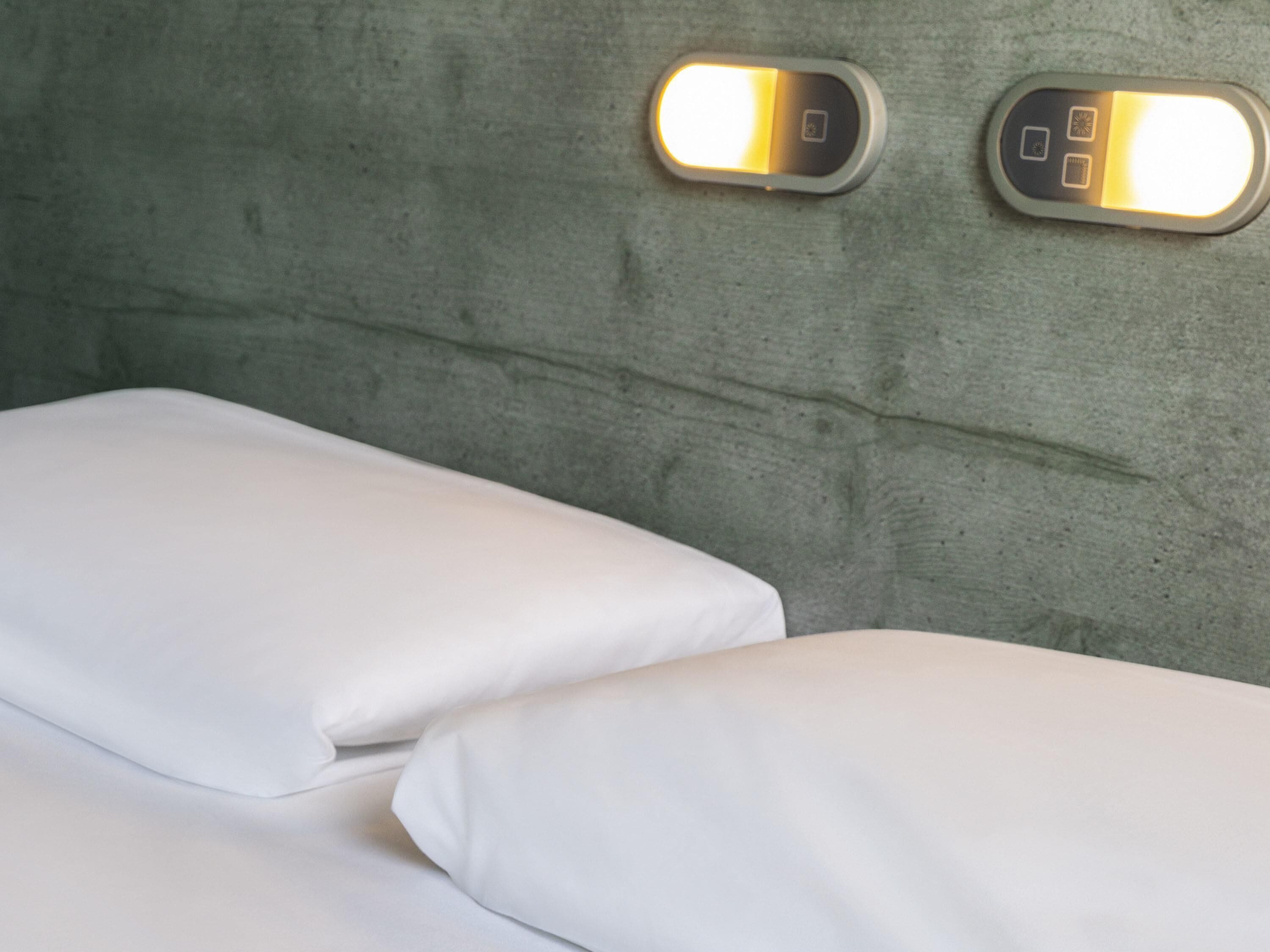 A bed with white linens and two wall-mounted light switches.