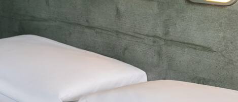 A bed with white linens and two wall-mounted light switches.