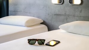 A hotel room with two beds, a pair of sunglasses, and a smartphone on the bed. - ibis budget Meudon Paris Ouest (Meudon)