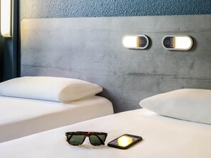 A hotel room with two beds, a pair of sunglasses, and a smartphone on the bed. - ibis budget Meudon Paris Ouest (Meudon)