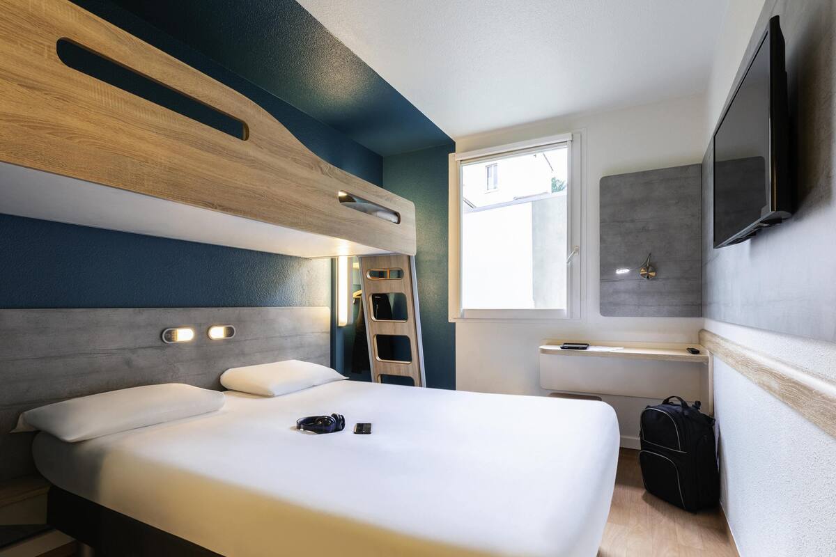 A modern hotel room with a bed, a TV, a window, and a luggage storage area.