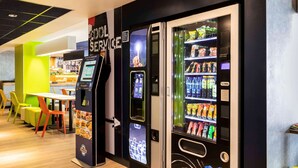 A modern indoor space with vending machines, a self-service kiosk, and a seating area with colorful chairs. - ibis budget Meudon Paris Ouest (Meudon)
