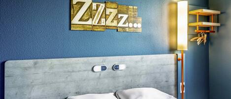 A hotel room with a bed, a headboard, a wall-mounted light, and a decorative wall piece.