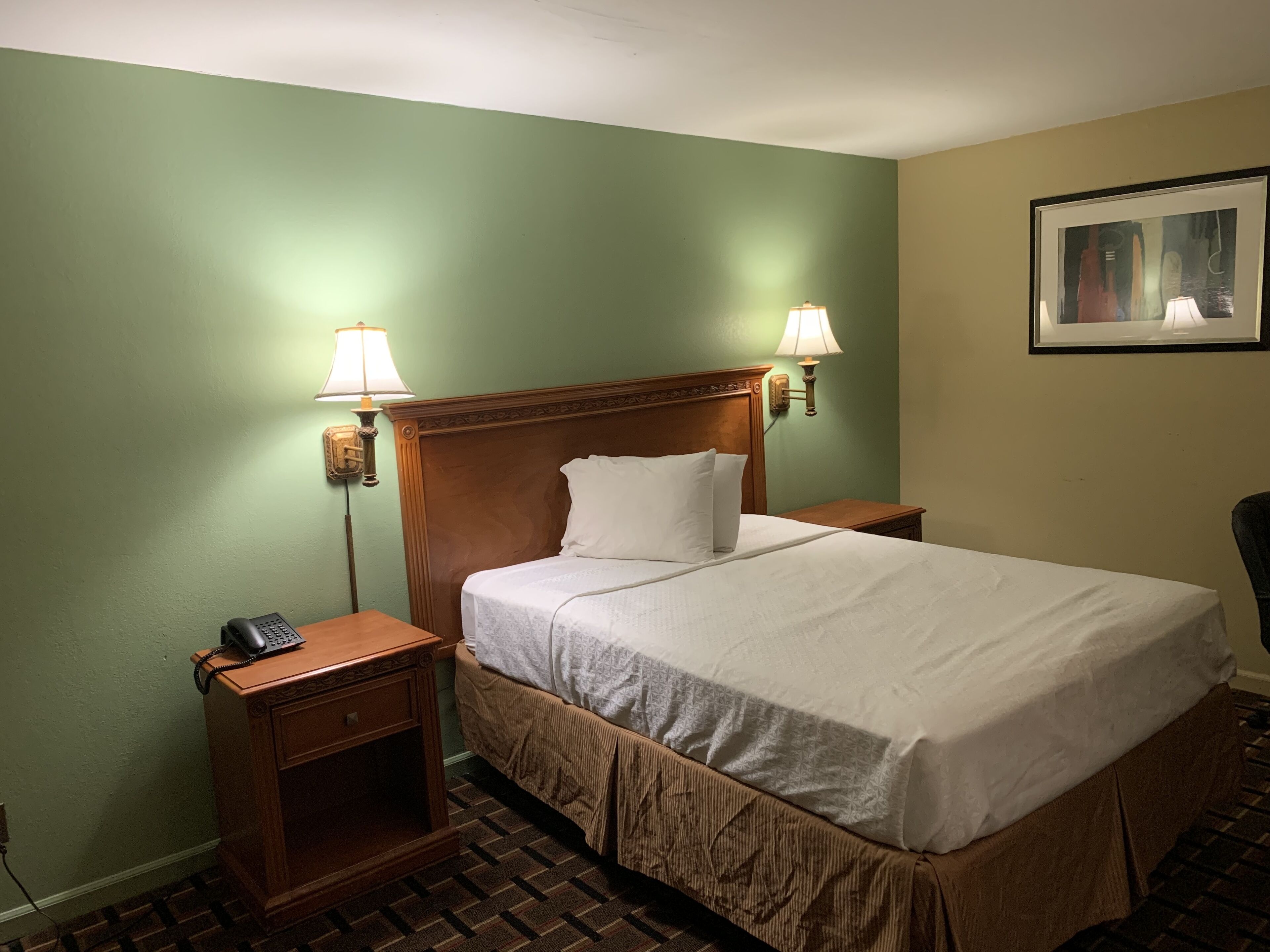 Quarto de hotel com uma cama grande, duas mesas de cabeceira, um telefone e duas luminárias na parede.