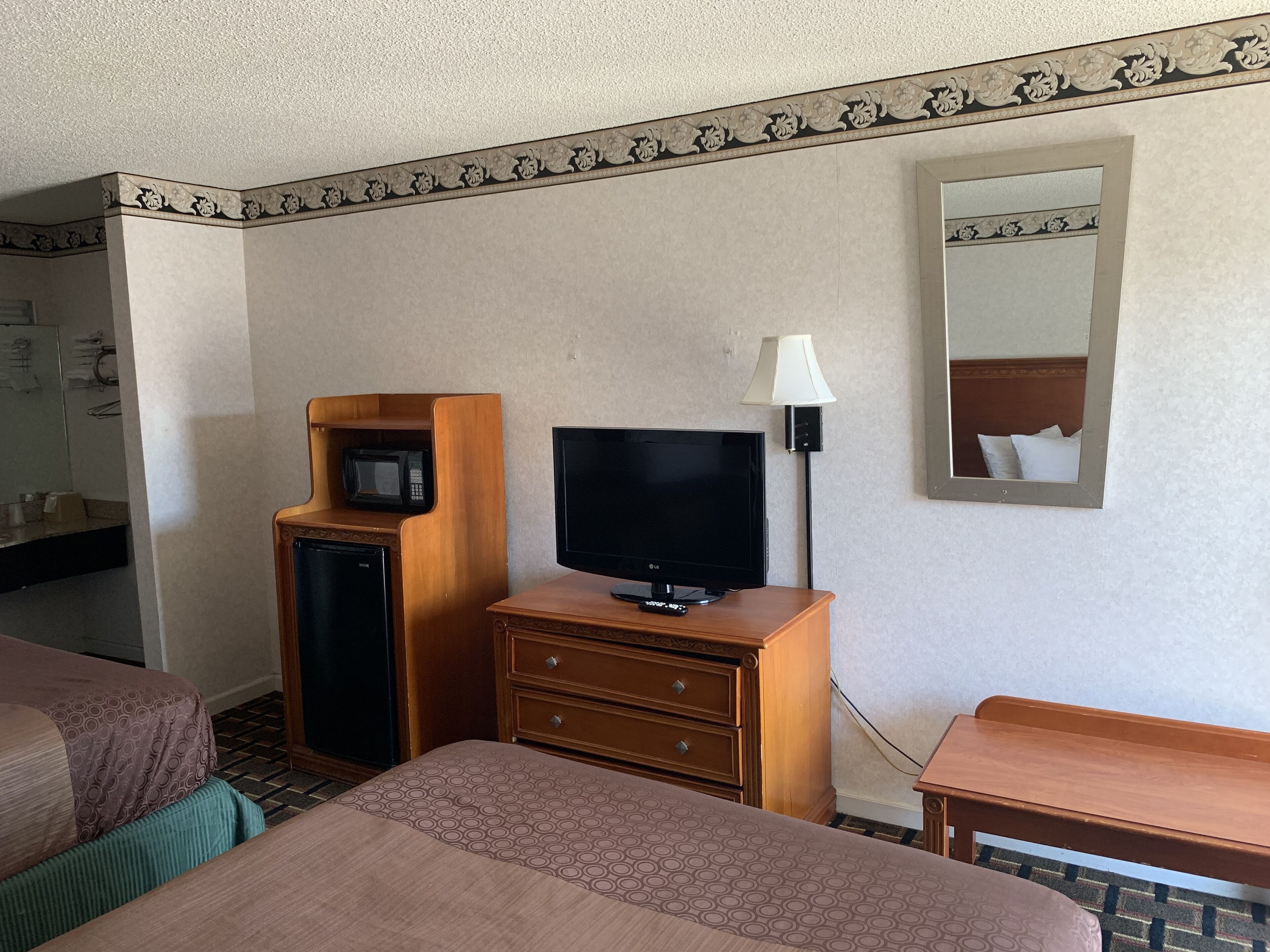 Habitación de hotel con cama, televisión, microondas, lámpara y espejo.