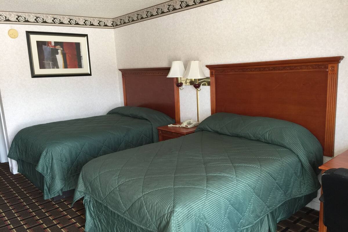 A hotel room with two single beds, a wooden headboard, a bedside table with a lamp, and a framed picture on the wall.