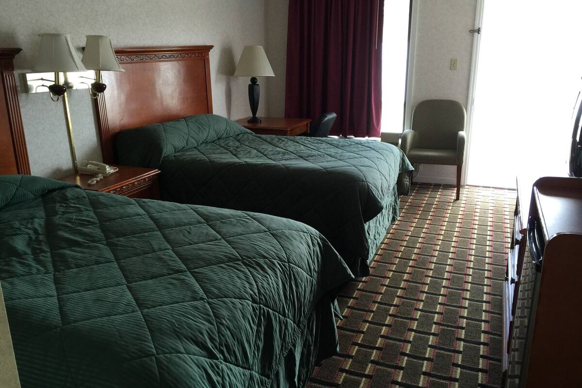 A hotel room with two beds, a desk with a telephone, a chair, a lamp, and a window with curtains.