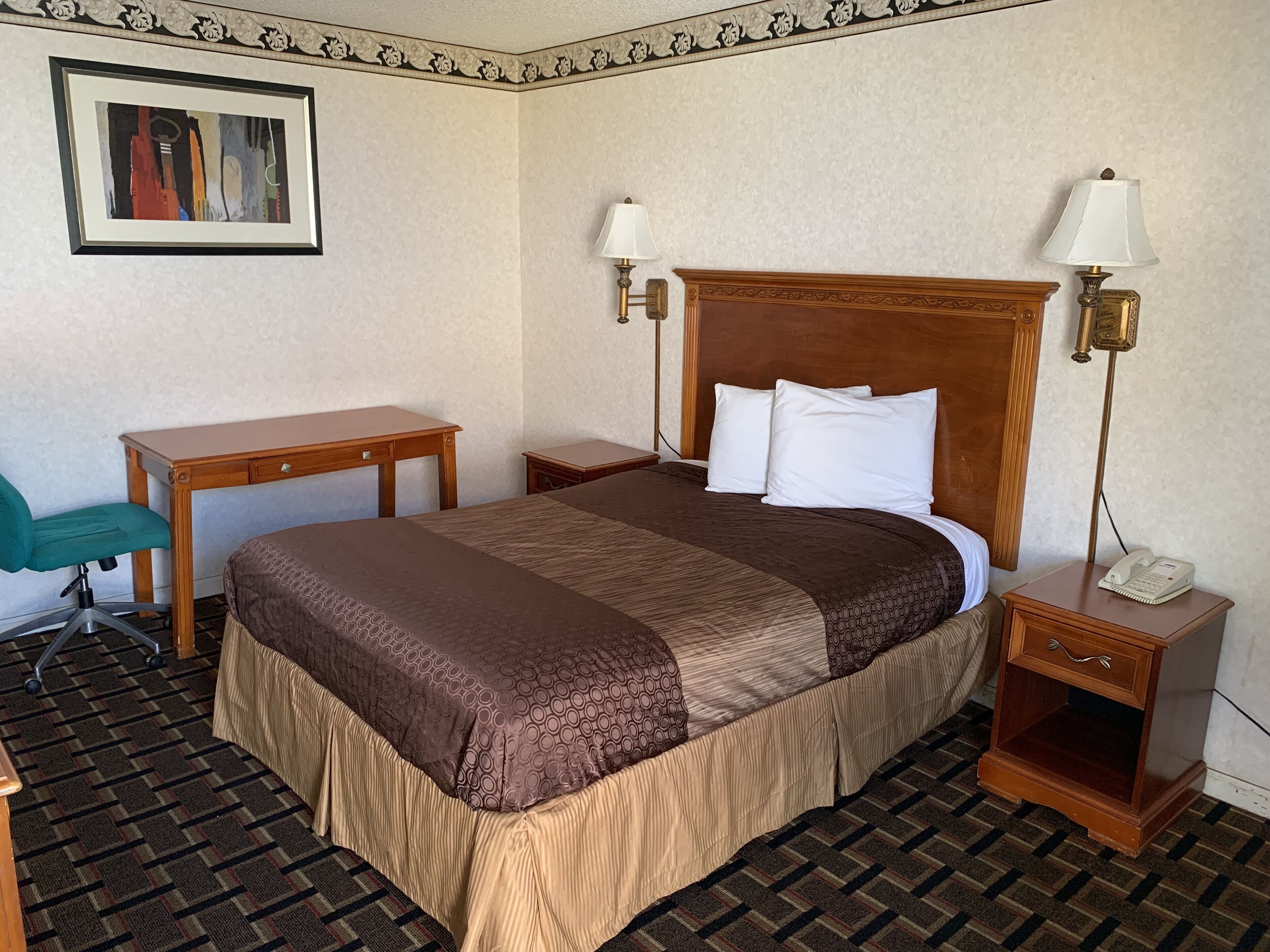 A hotel room with a large bed, two bedside tables, a desk, a chair, and a painting on the wall.